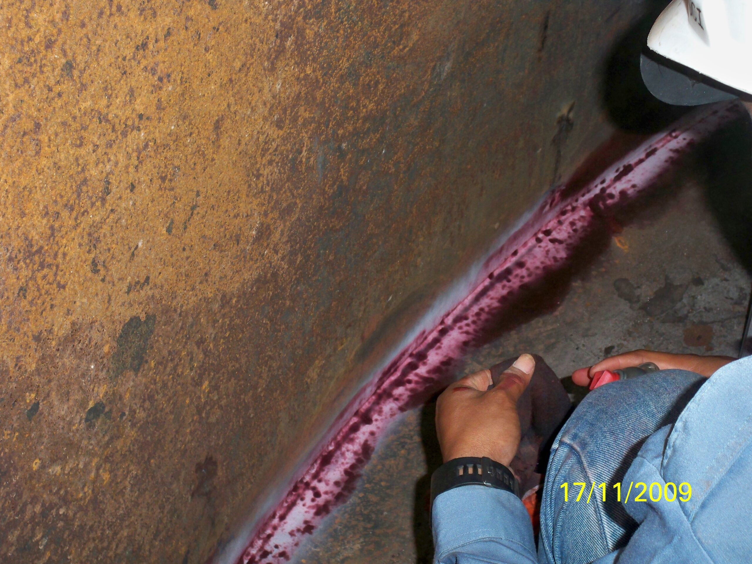 Teknisi sedang melakukan Dye Penetrant Test (DPT) pada jalur pengelasan di dalam tangki.