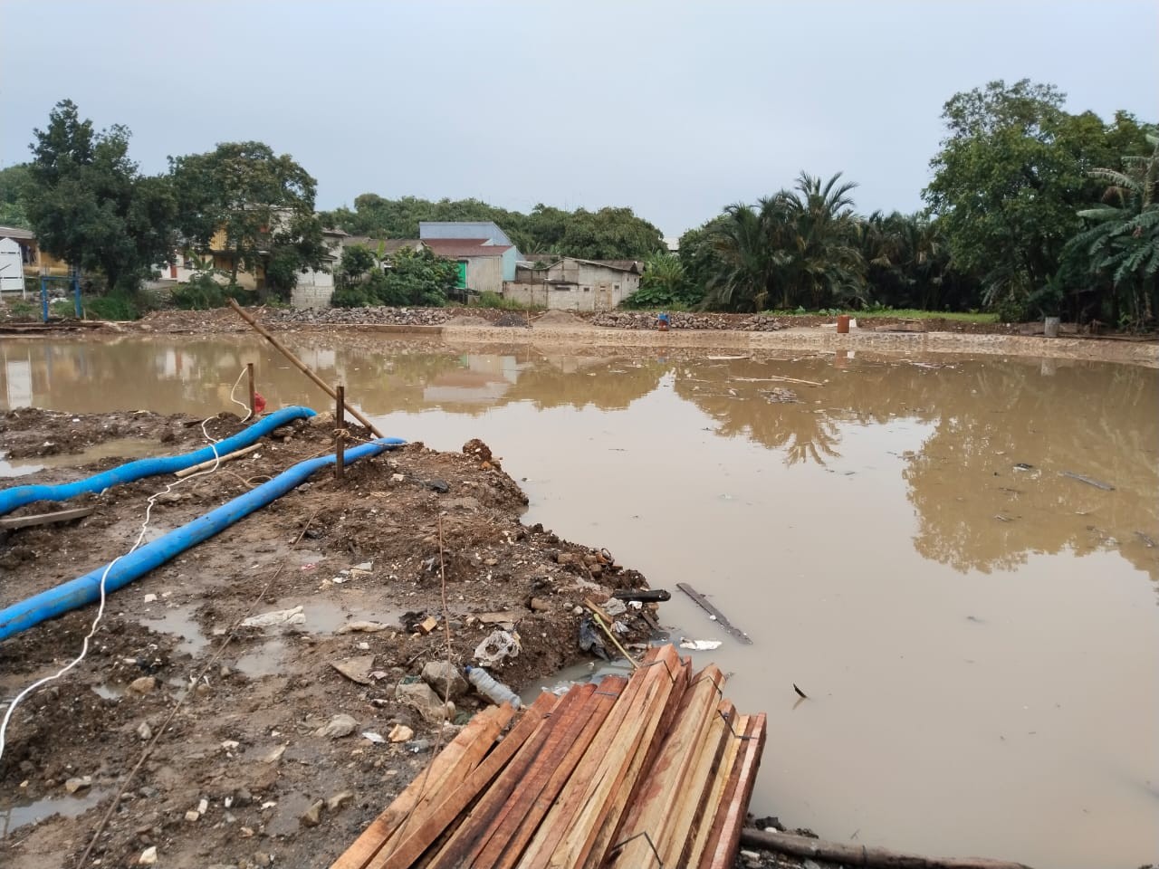 Instalasi pipa discharge fleksibel berwarna biru di lokasi proyek dewatering
