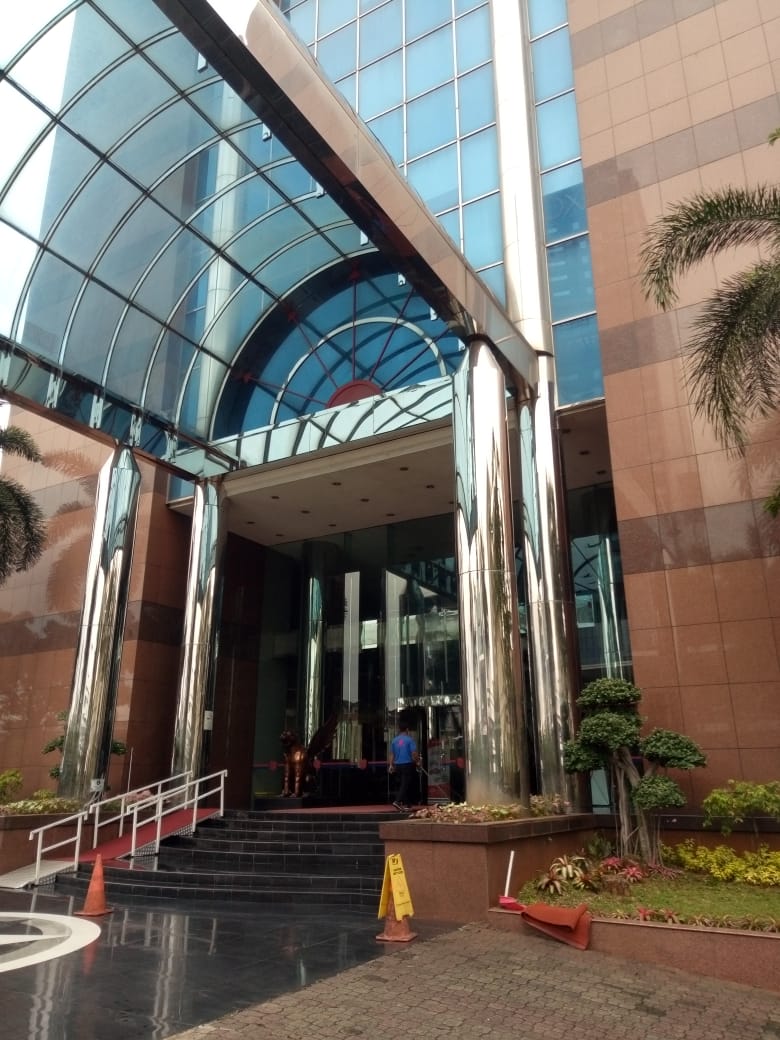 Pintu masuk utama gedung perkantoran dengan kolom berlapis stainless steel yang menjadi titik tumpu struktur kanopi baru.