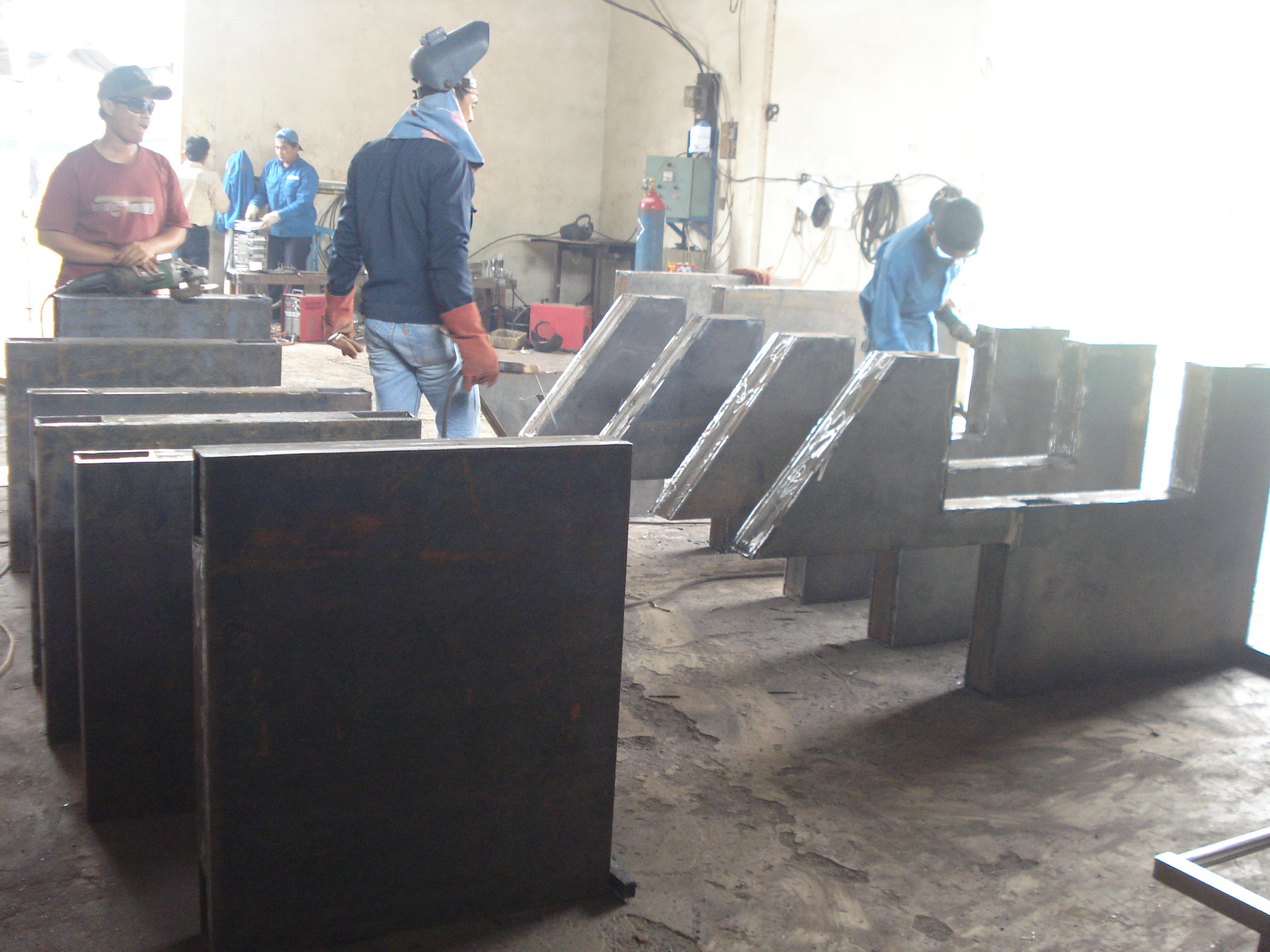 Aktivitas di workshop fabrikasi dengan beberapa teknisi sedang mengerjakan rangka baja kabin robot