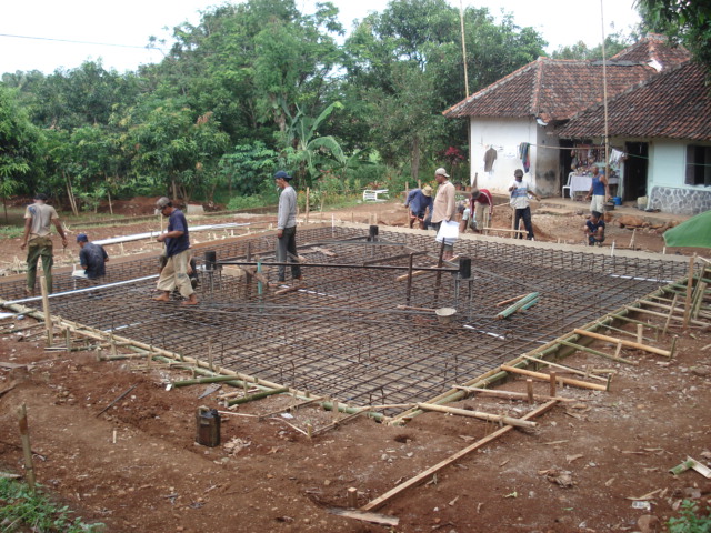 Tim kerja sedang melakukan instalasi tulangan baja (rebar) untuk fondasi.