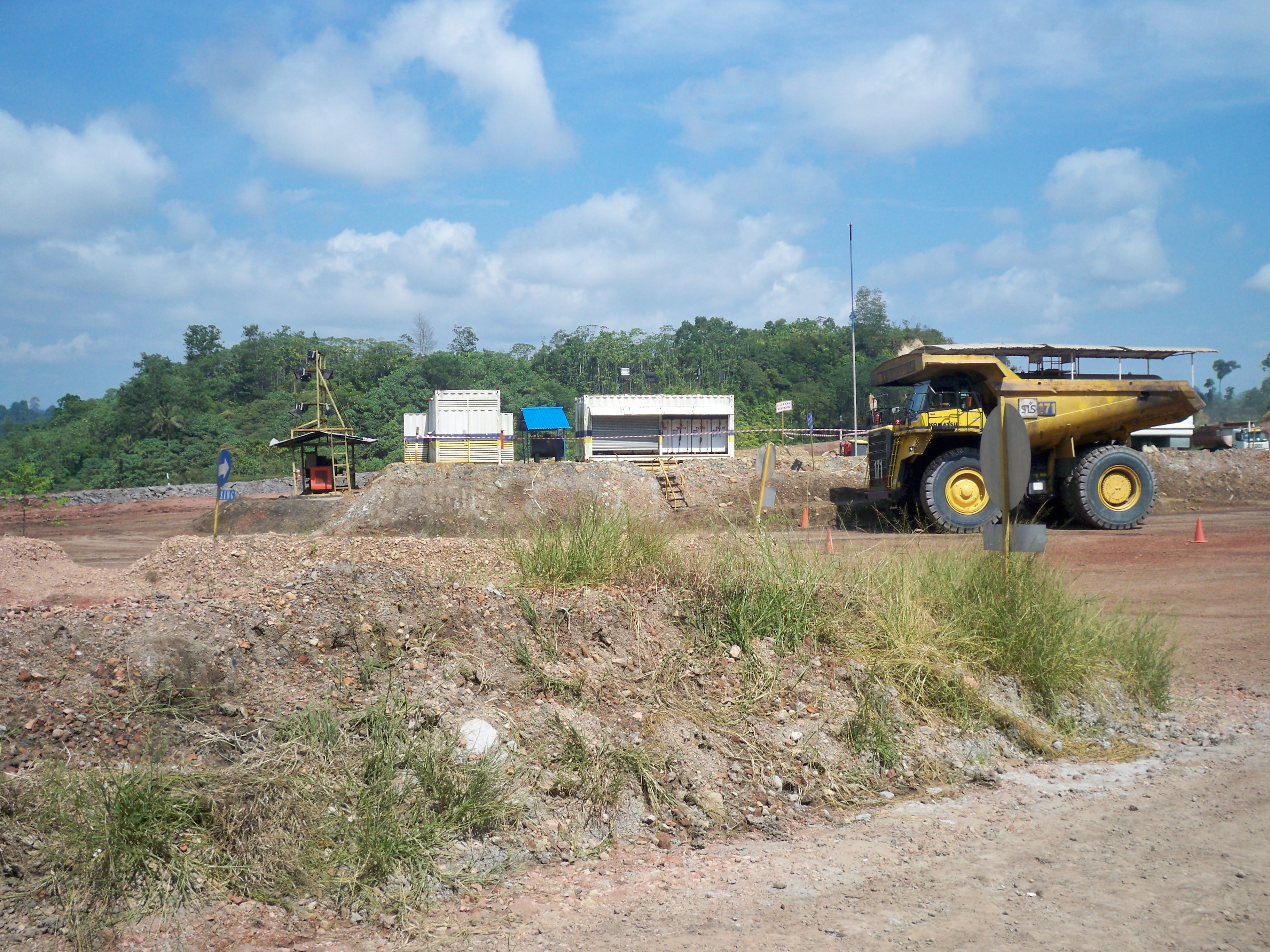 Area operasional tambang terbuka dengan alat berat dan fasilitas sementara.